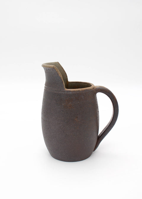 A dark brown ceramic pitcher with a textured glaze, a small integrated lid, and a curved handle, shown on a seamless white background.